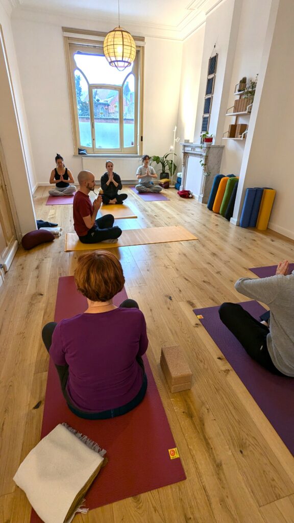 Moment d'introspection lors d'une séance de Yoga à Braine-le-Comte. Les participants sont en tailleurs et joignent leurs mains. 